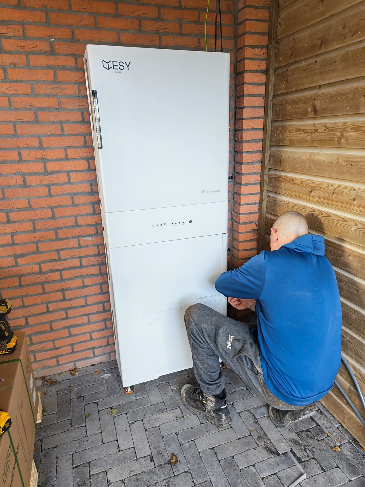 Onze monteur sluit de onderste batterijmodule van een ESY HM15 aan onder een overkapping, met de bekabeling langs de gevel weggewerkt.